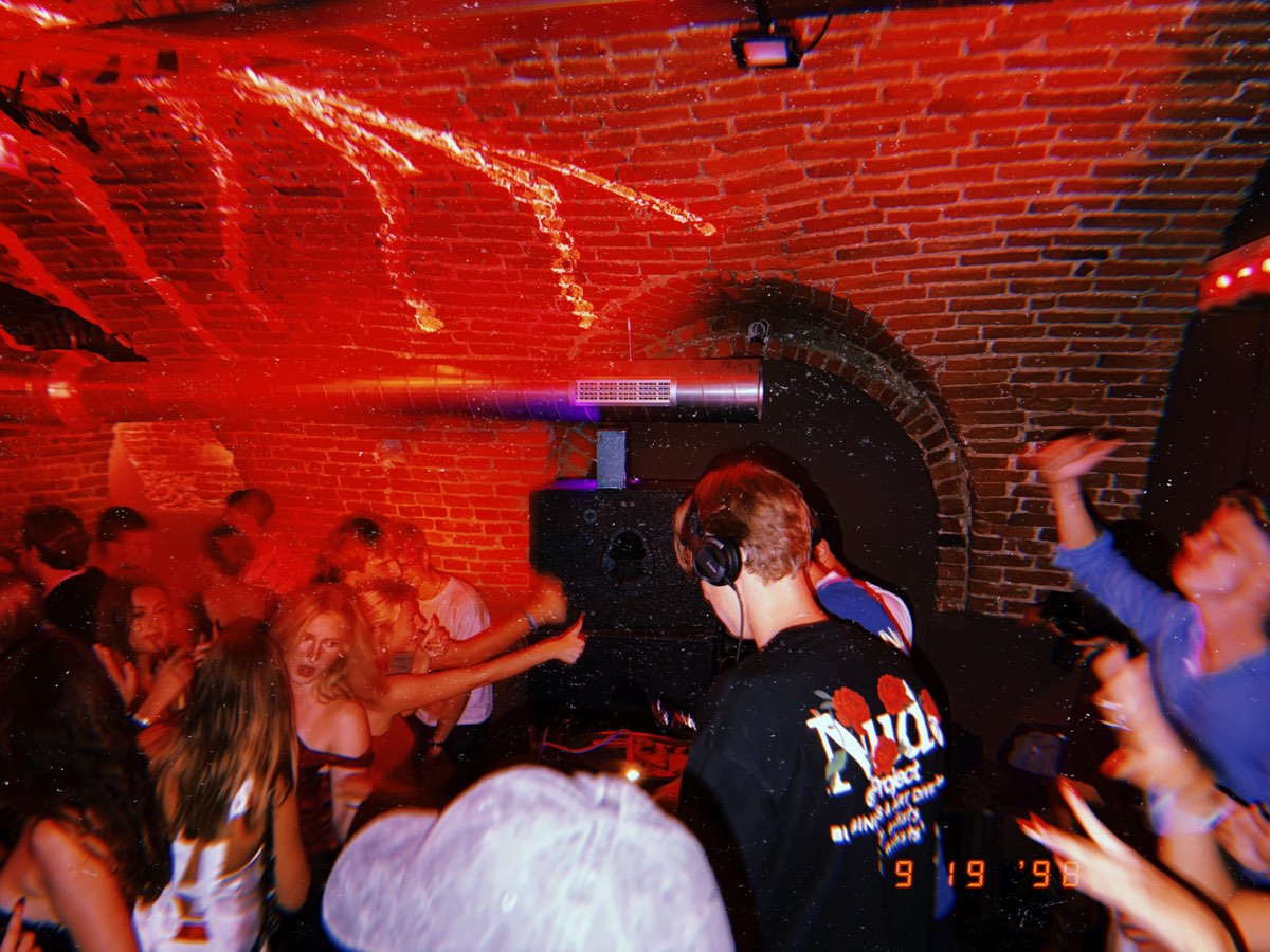 behind the decks under red light, the crowd pressed close against the booth